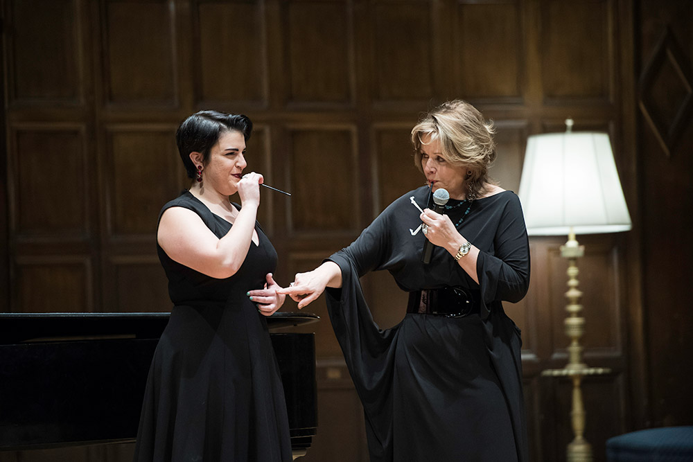 two opera singers on stage, one instructing the other, pointing to her diaphragm