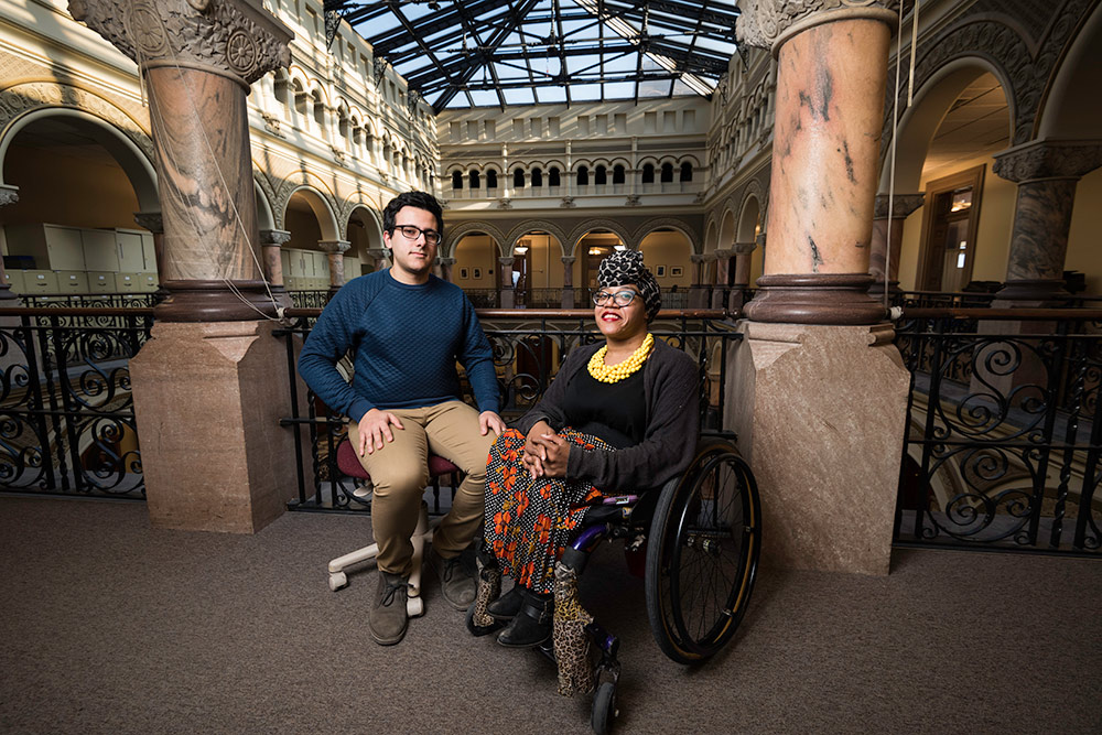 young man and woman in a wheelchair pose for a photo in City Hall