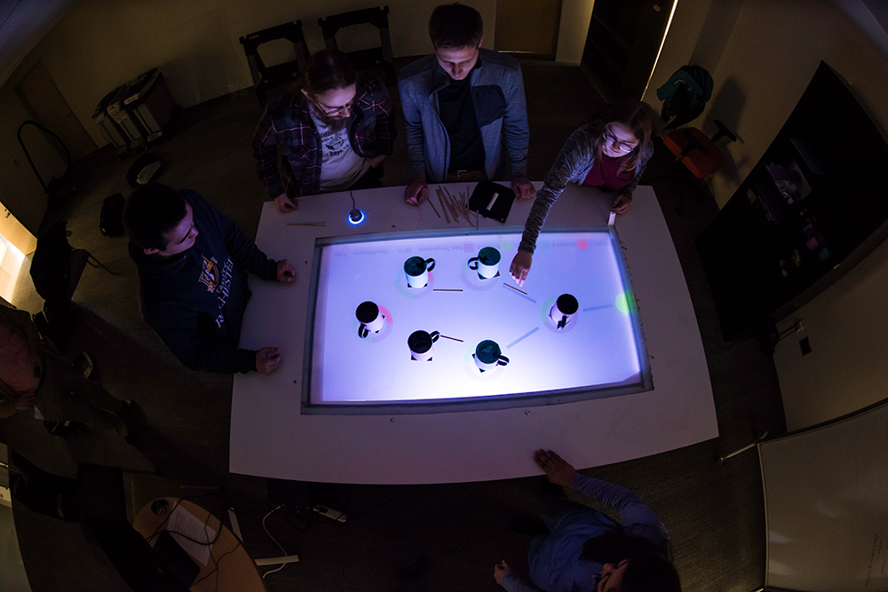 students moving coffee mugs around on a lighted table surface