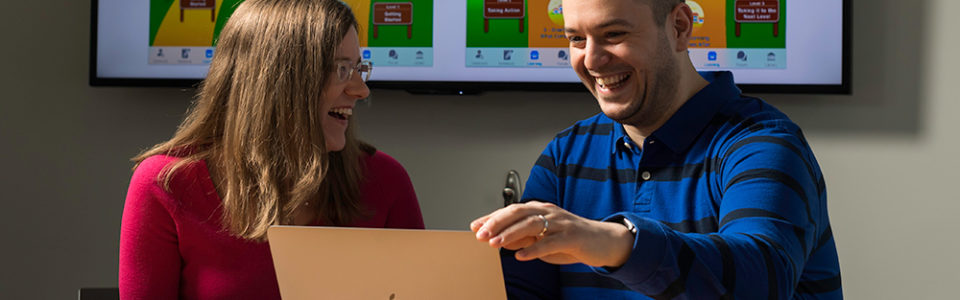 two researchers looking at a laptop and smiling