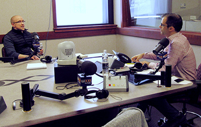 two people in a radio studio, speaking into microphones