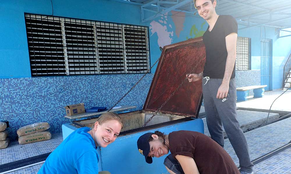 three students posing in front of a large blue storage shed.