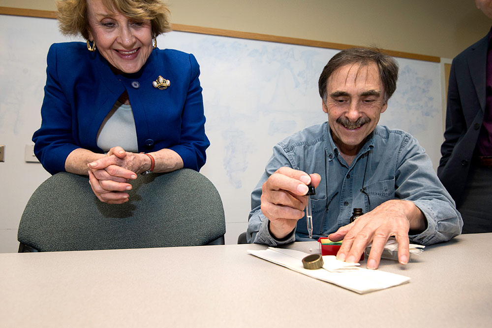 Louise Slaughter laughs and looks on as scientist drops water onto a new material