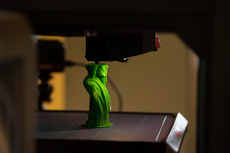 3d printer has created two-thirds of a small green statue of Frederick Douglass