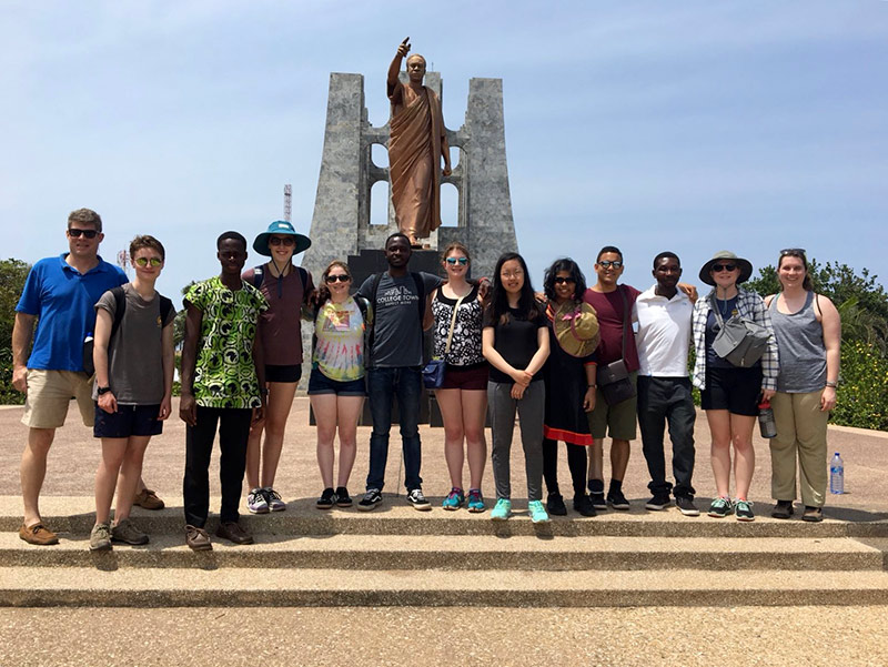 group of students posing in front of a large statue