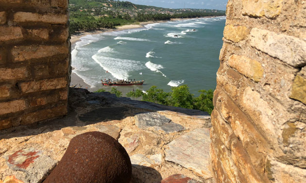 a long canoe launching into a bay in Elmina, viewed from the turret of Fort Amsterdam