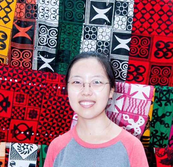 woman smiles and poses in front of colorful textiles