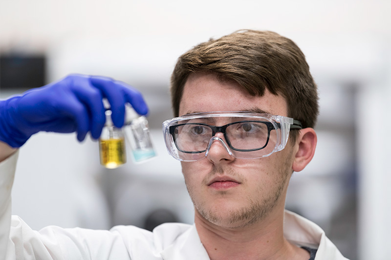 student with lab coat and goggle holding up test tubes