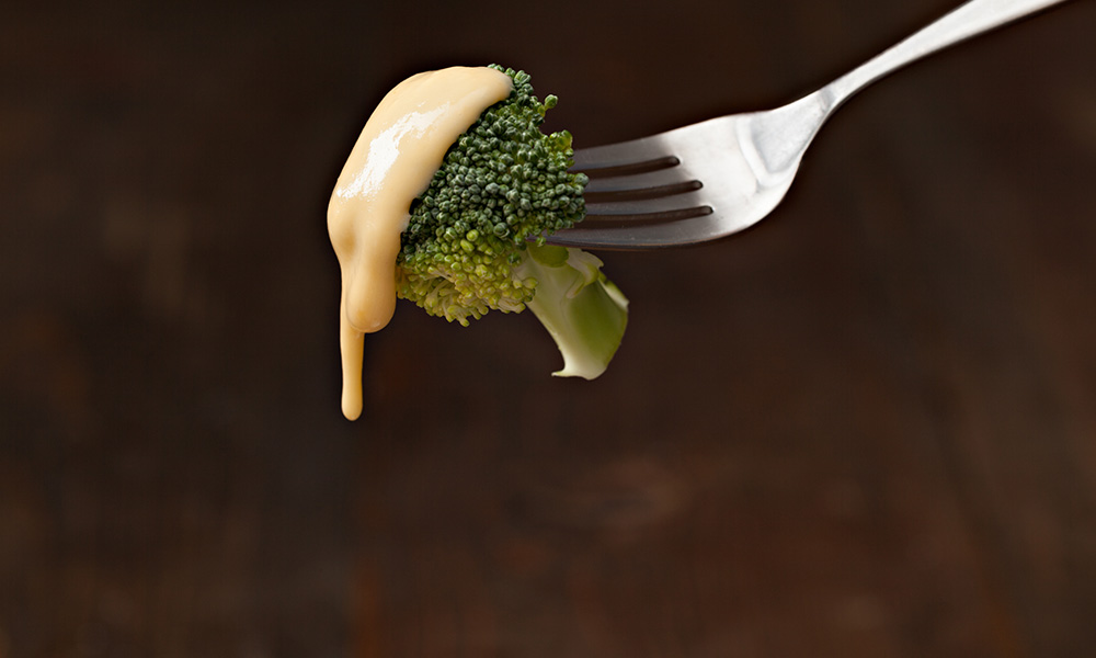 cheese sauce dripping off a piece of broccoli to illustrate lipid droplets.