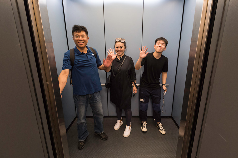 student and his parents wave from inside an elevator