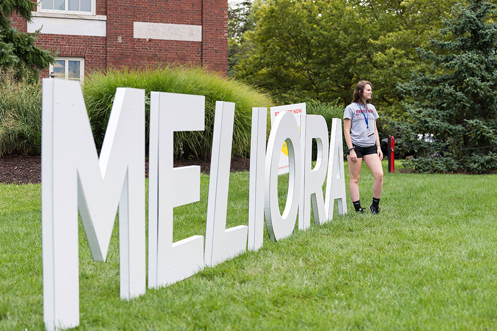 student stands in front of large letters that read MELIORA