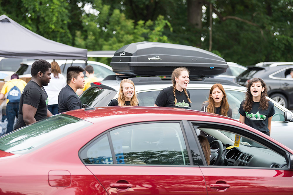 group of students singing for people waiting in a row of cars