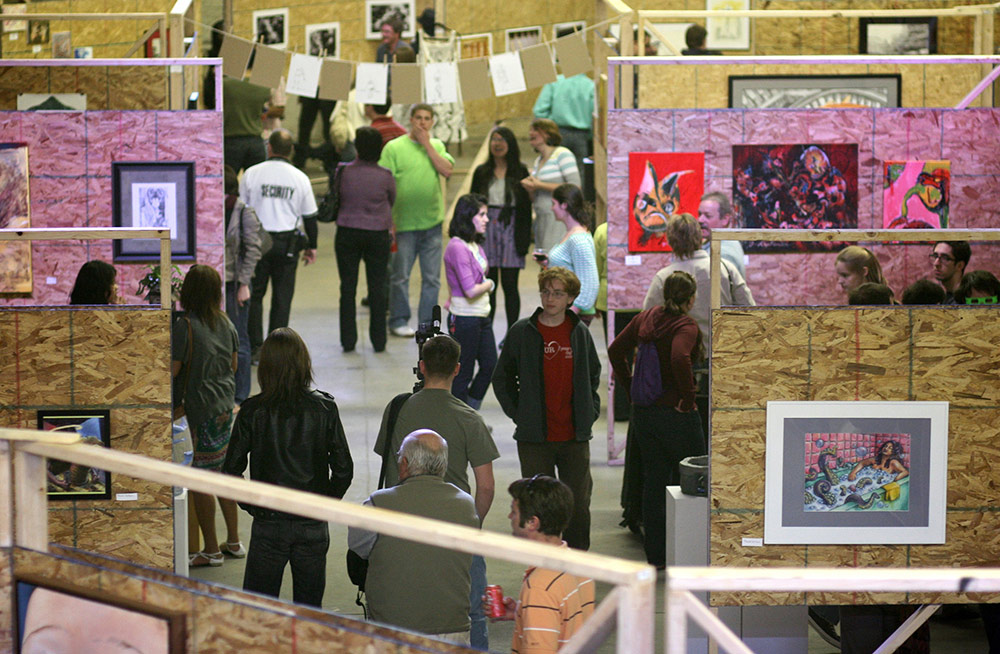 large group of people viewing paintings and other artworks in a large warehouse space