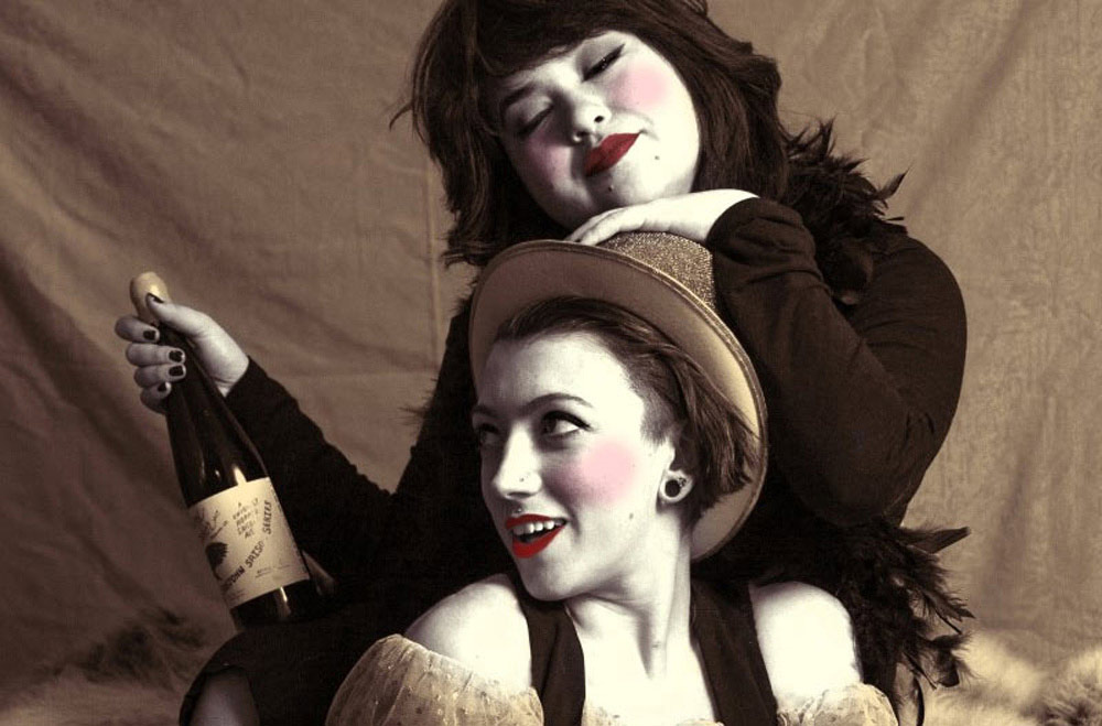 close-up of two artists in costume and makeup, one holding a bottle of wine