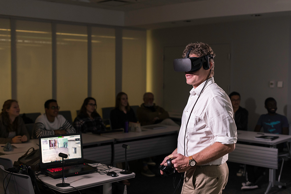 Michael Jarvis in front of a classroom of students, wearing a virtual reality headset