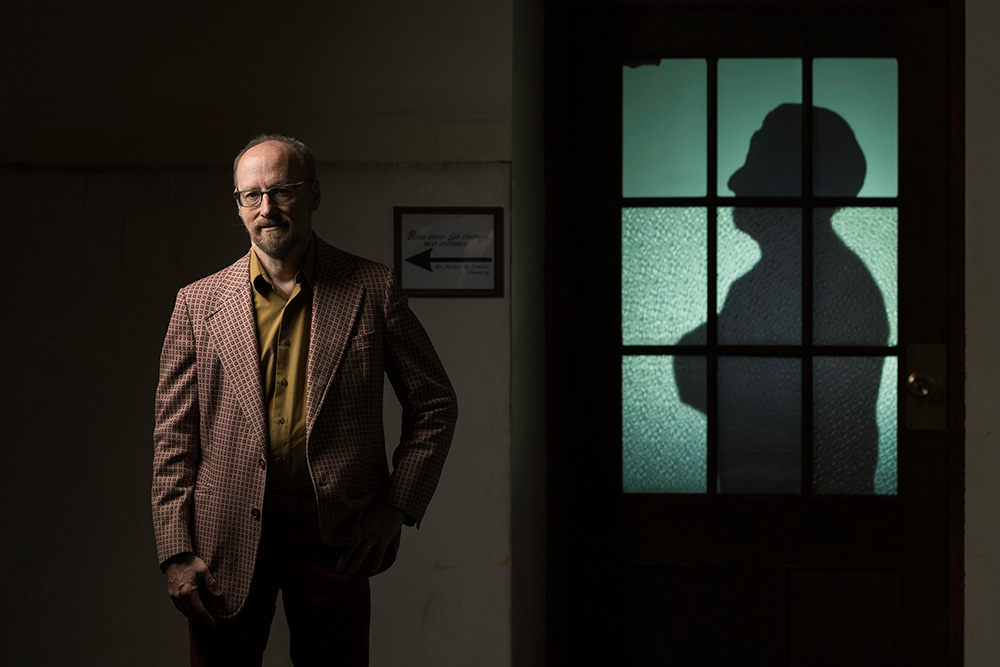 artist Allen Topolski stands next to a classroom door, lit from behind and showing the silhouette of a person