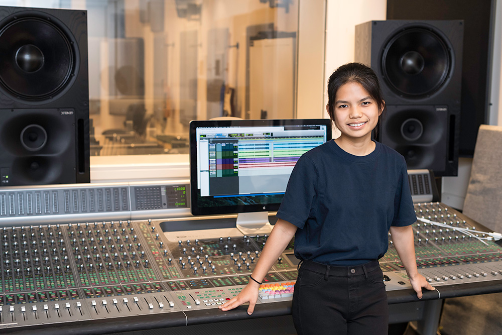student stands in front of a large sound board
