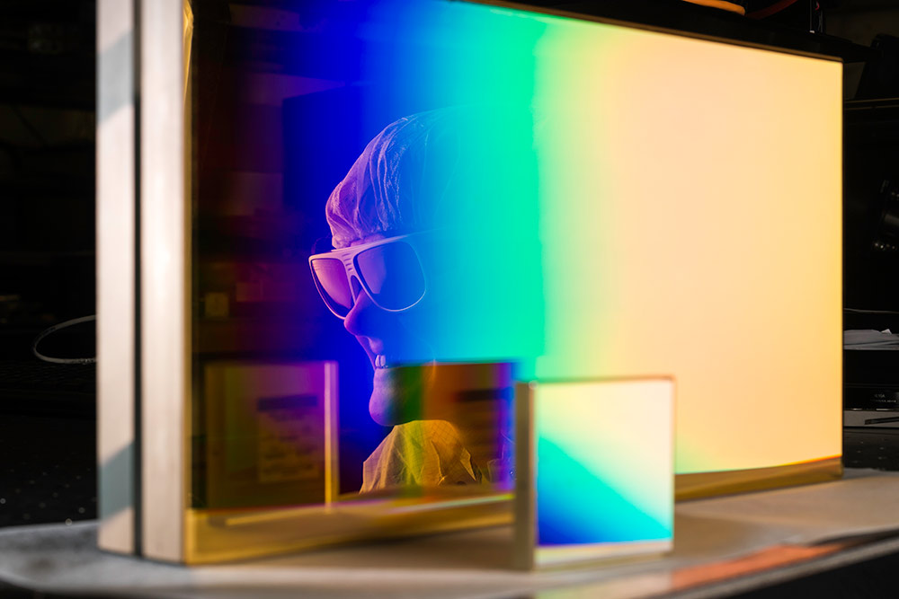 a woman's face reflected in the colorful surface of a large piece of glass, with a smaller square piece of glass in the foreground.