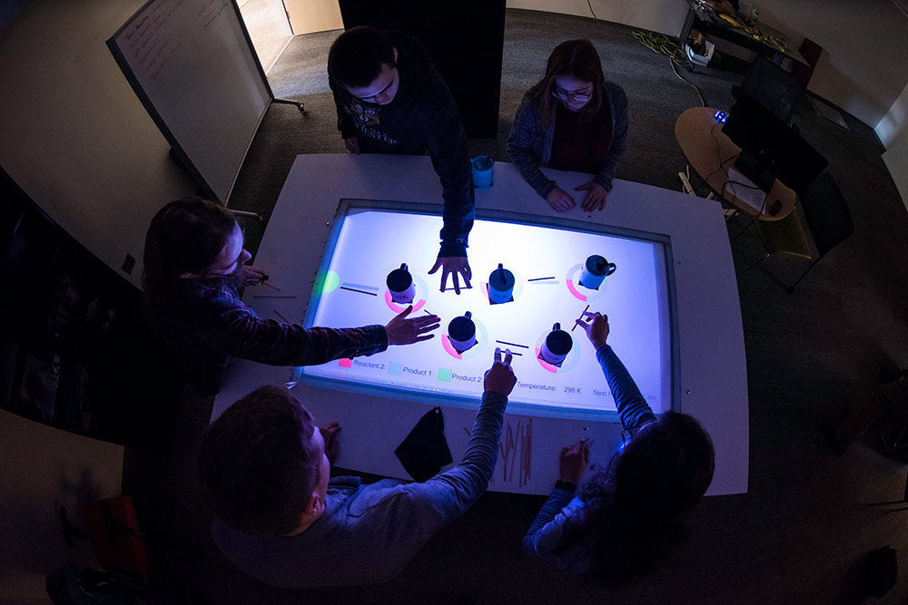 overhead shot of a lighted table with hands reaching out over it to move mugs across it. 