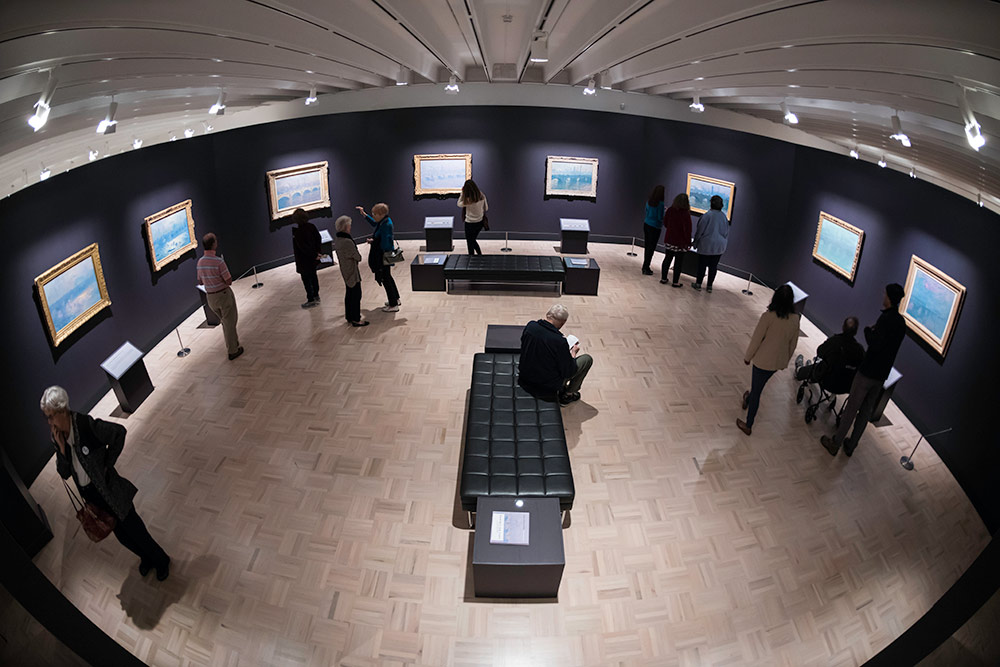 fish-eye lens view of an art exhibition with eight Monet paintings on the walls of a museum.