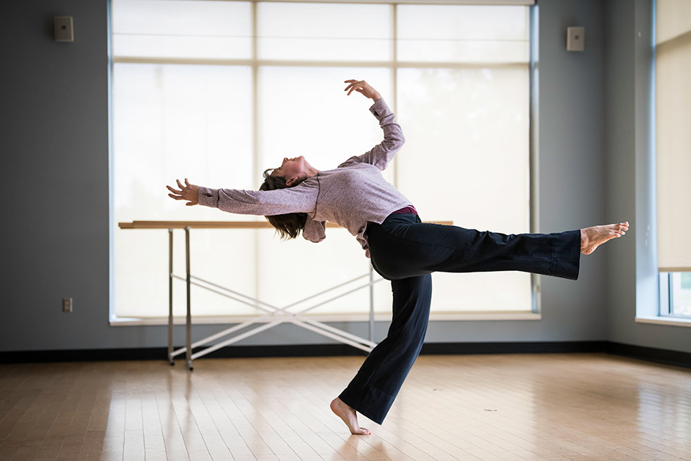 Missy Pfohl-Smith in a dance studio, leaning back and reaching over her head. 