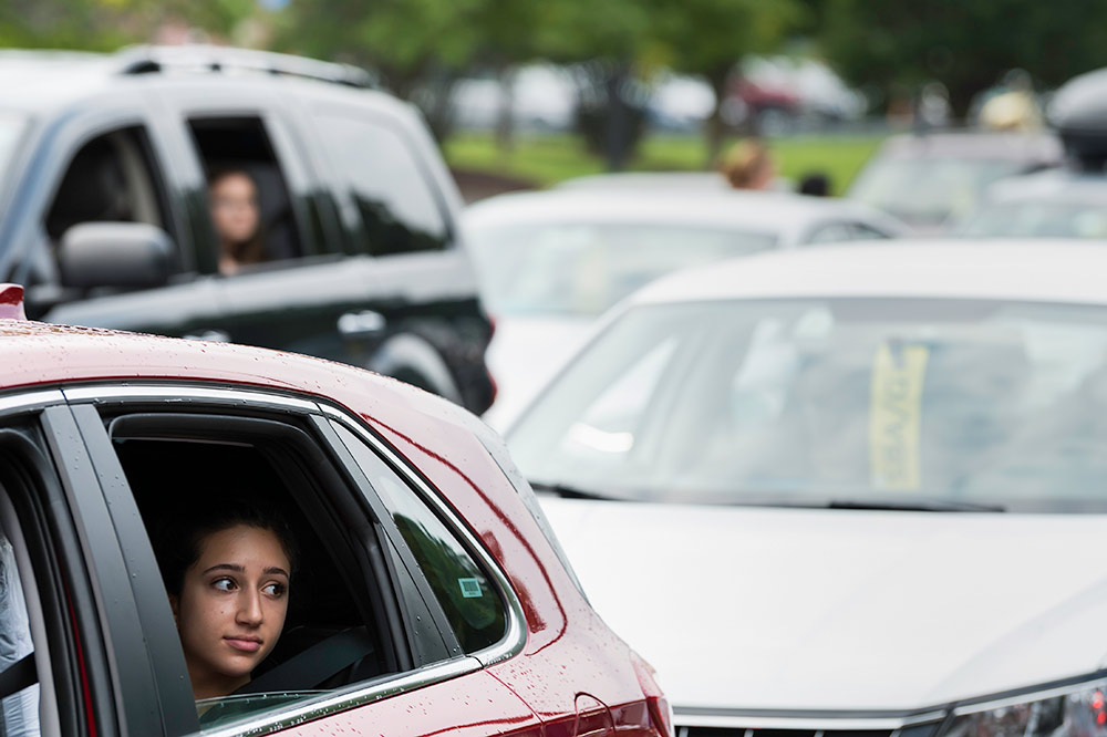 student looks out the window of a car, with a line of cars behind her.