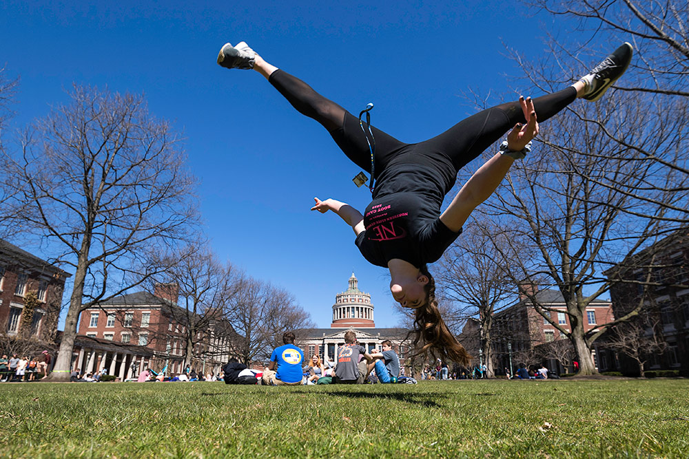 student appears suspended upside down in mid air, with the library tower in the background.