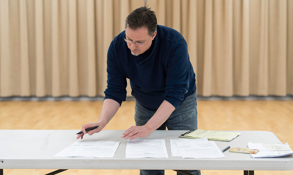 Nigel Maister, sorting through pages of a script scattered across a table.