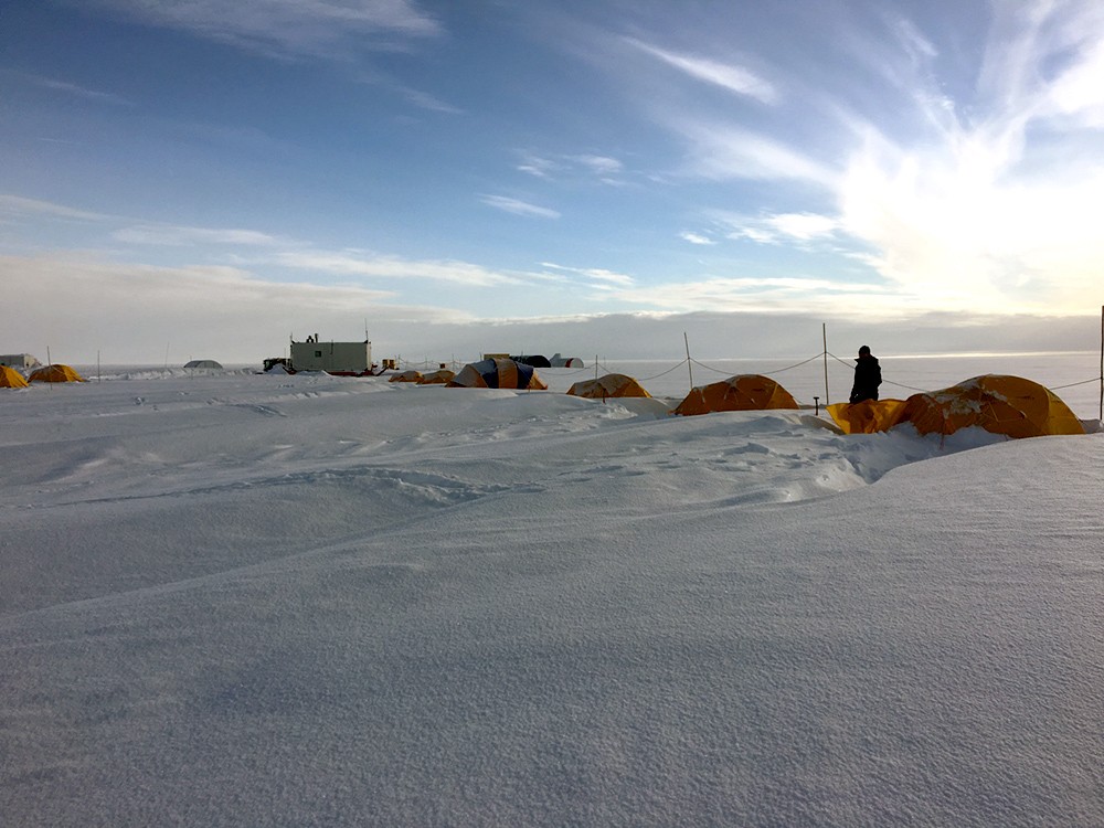 sunset over a camp of tents on a vast field of ice and snow.