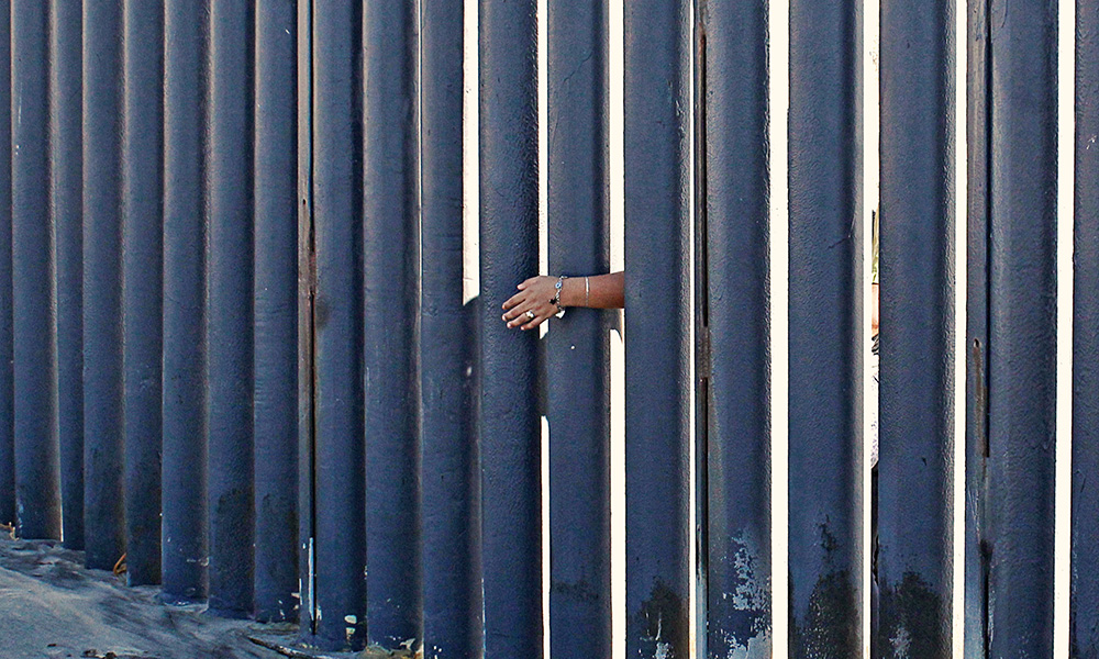 person's single hand reaching through a border fence.