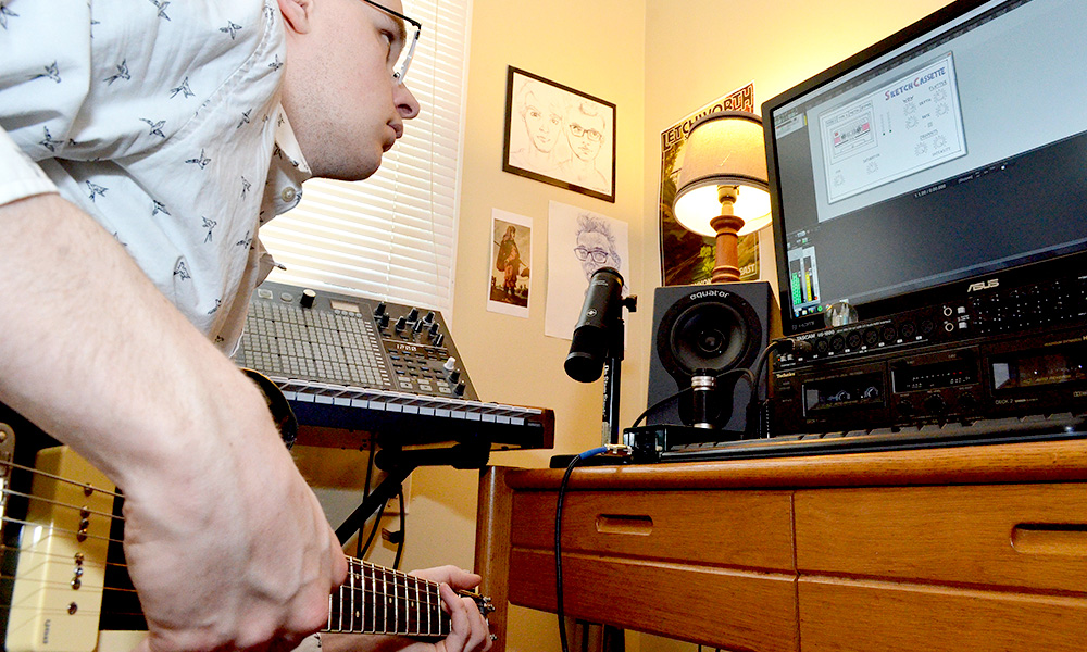 student playing a guitar and looking at a computer screen with the Skethcassette plugin interface on the screen.