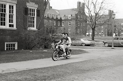 archival photo of two people riding a motorcycle on River Campus