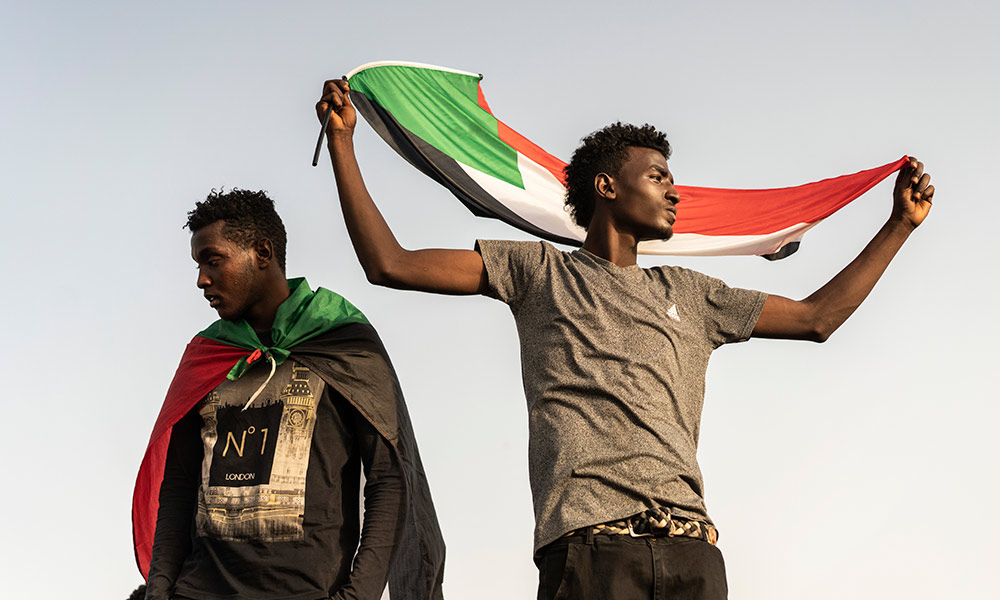 two protesters in Sudan, one holding a Sudanese flag.