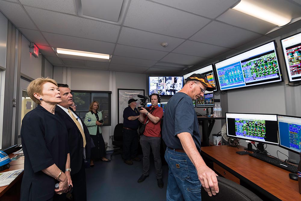group of people in a control room looking at data on a bank of large computer screens.