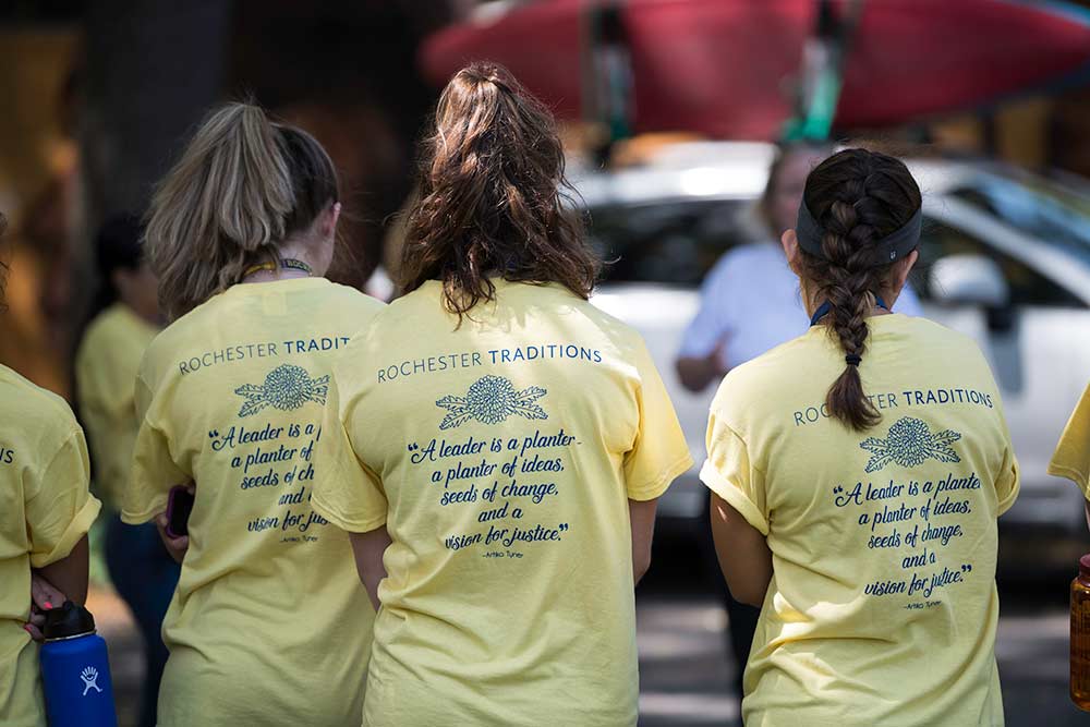 three people wearing t-shirts that read ROCHESTER TRADITIONS. A LEADER IS A PLANTER, A PLANTER OF IDEAS, SEEDS OF CHANGE, AND A VISION FOR JUSTICE. -- ARTIKA TYNER