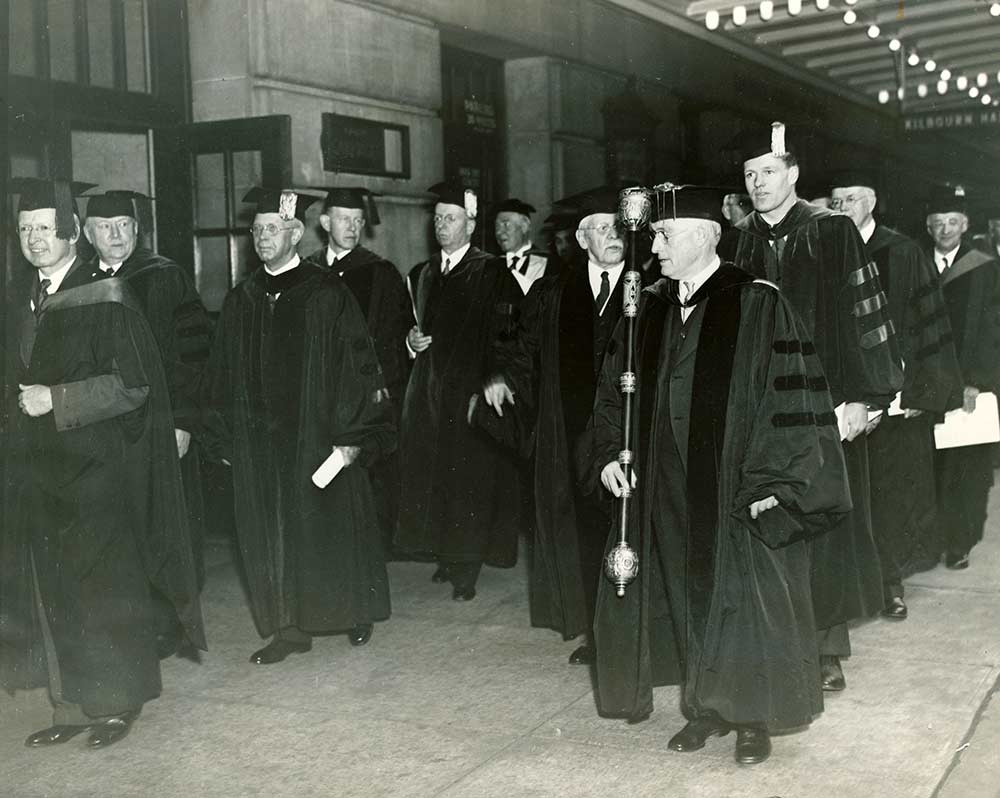 archival photo of procession ofpeople in cap and gown outside Eastman Theatre