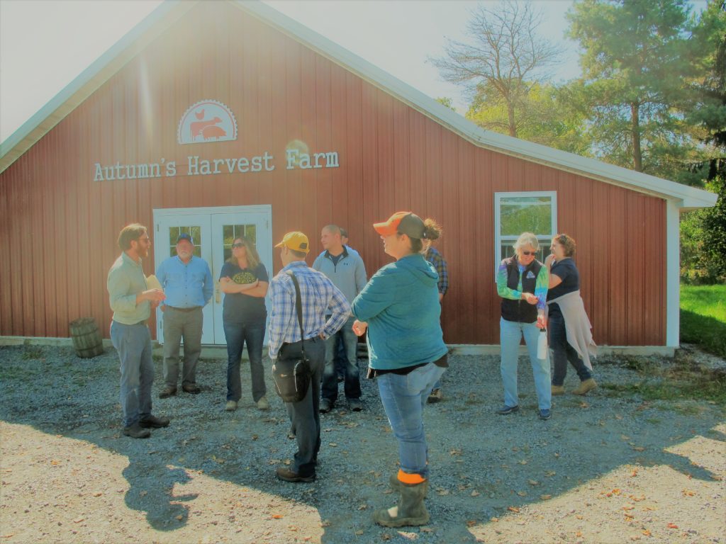 students taking a tour stand in front of a barn painted with a sign that reads Autumn's Harvest Farm