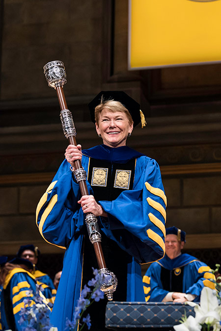 President Sarah Mangelsdorf in academic regalia holding the mace.