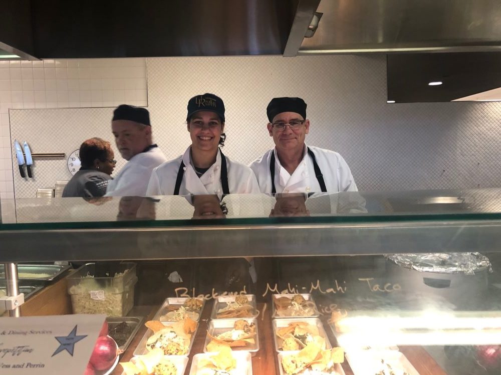 two public safety officers in chef uniforms smile from behind kitchen counter.