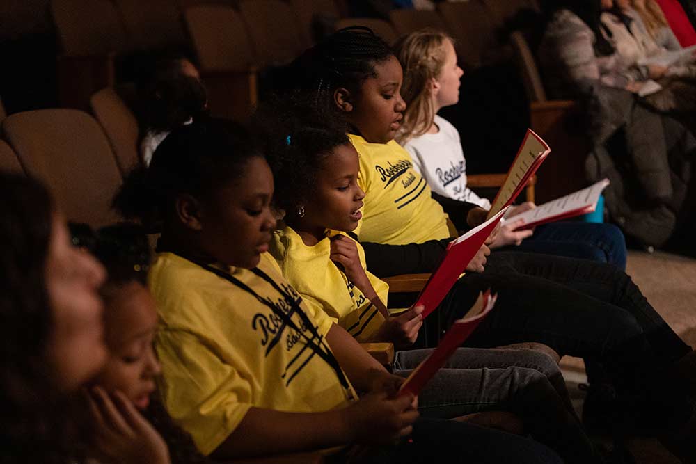 row of kids in a theatre audience sing from their programs.