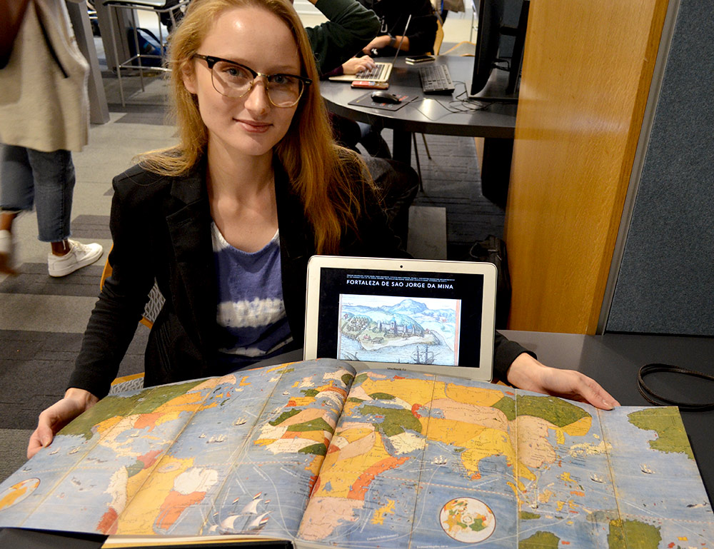 students holds a large map of the world and a tablet computer.