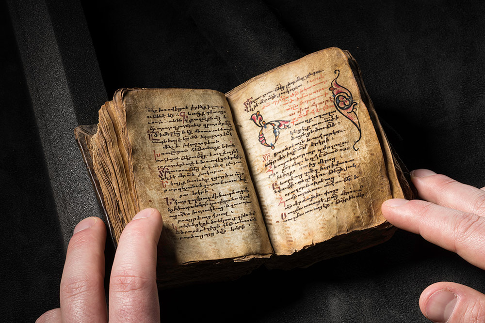 small ancient book, with someone's fingers holding it open to a handwritten page
