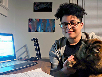 student with cat sits at desk with laptop.