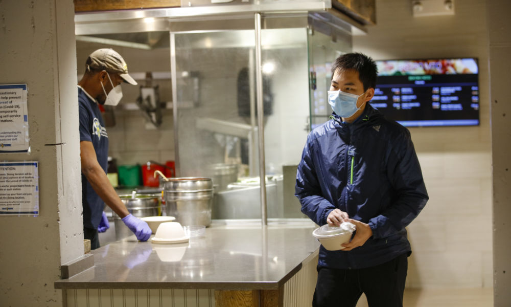 student and dining hall staff member in dining hall, both wearing masks
