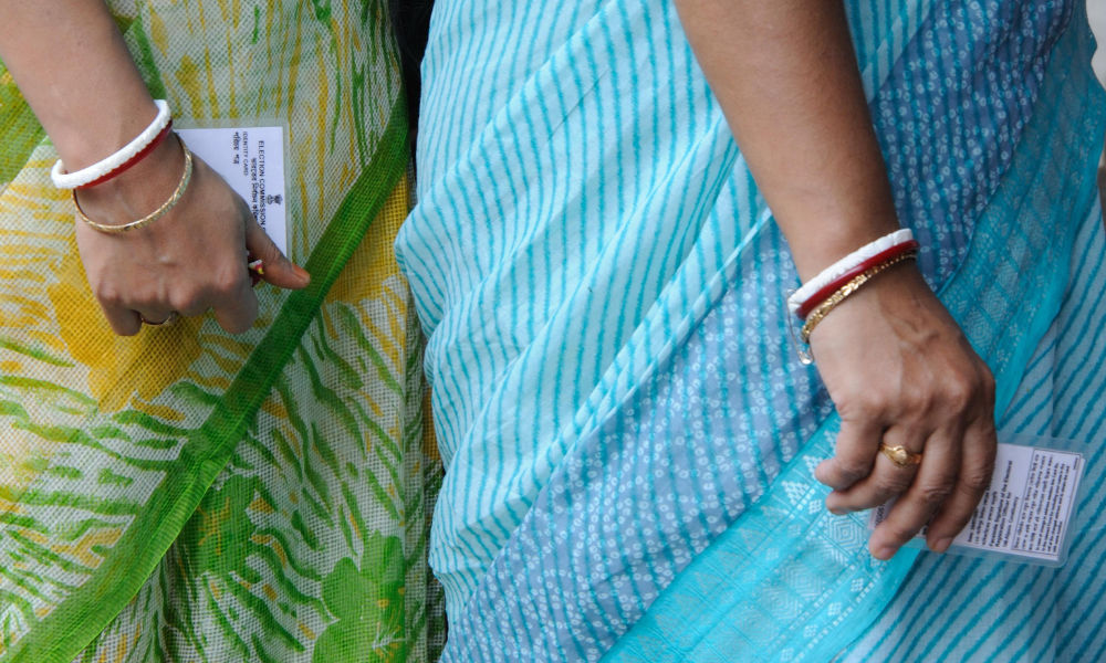 close-up of two Indian women in saris holding election cards.