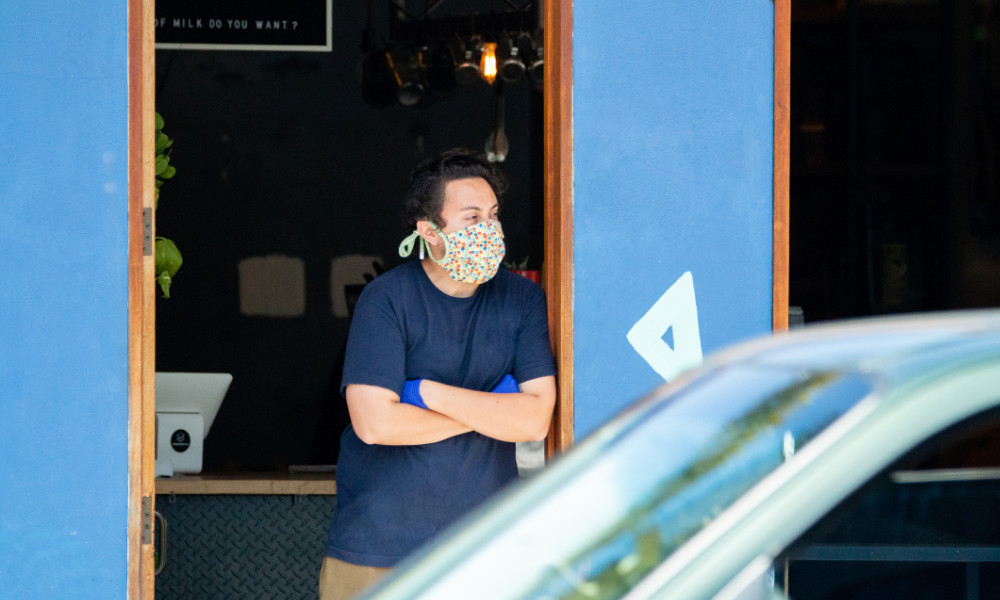 man in fask mask leans against the door of a shop.