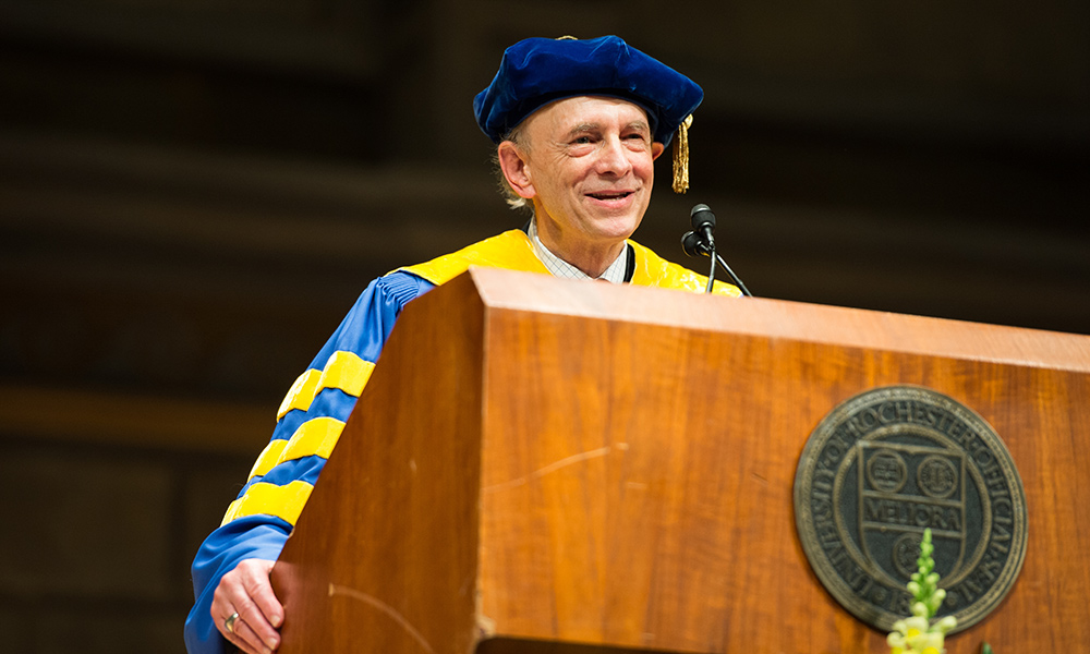 person in academic regalia giving a speech at a Rochester commencement ceremony.