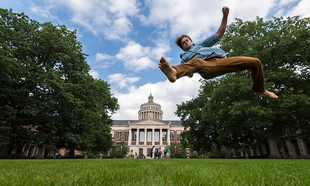 student does a leap on the quad that makes it look like he is jumping over Rush Rhees Library.