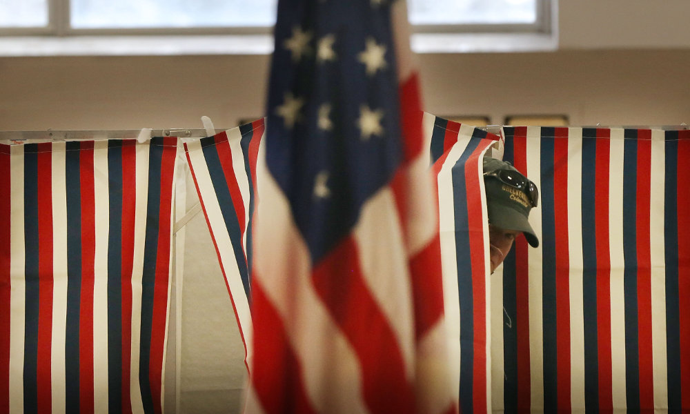 Voter peers from behind ballot curtain with an American flag in foreground.