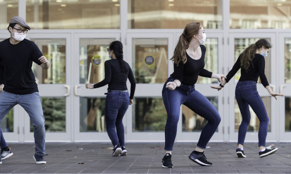 Students wear jeans and black tops while dancing on Wilson Commons porch.